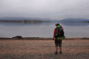 Back view of walker with backpack on lochside beach